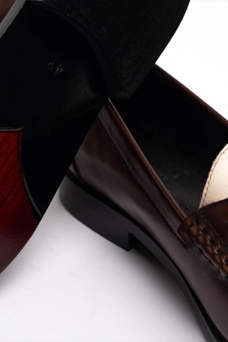 Pu&ograve; includere: Primo piano di un paio di mocassini in pelle marrone. Le scarpe hanno un design classico con una finitura lucida. Le suole sono nere e l'interno &egrave; di colore chiaro. La taglia 42 &egrave; visibile sulla suola.