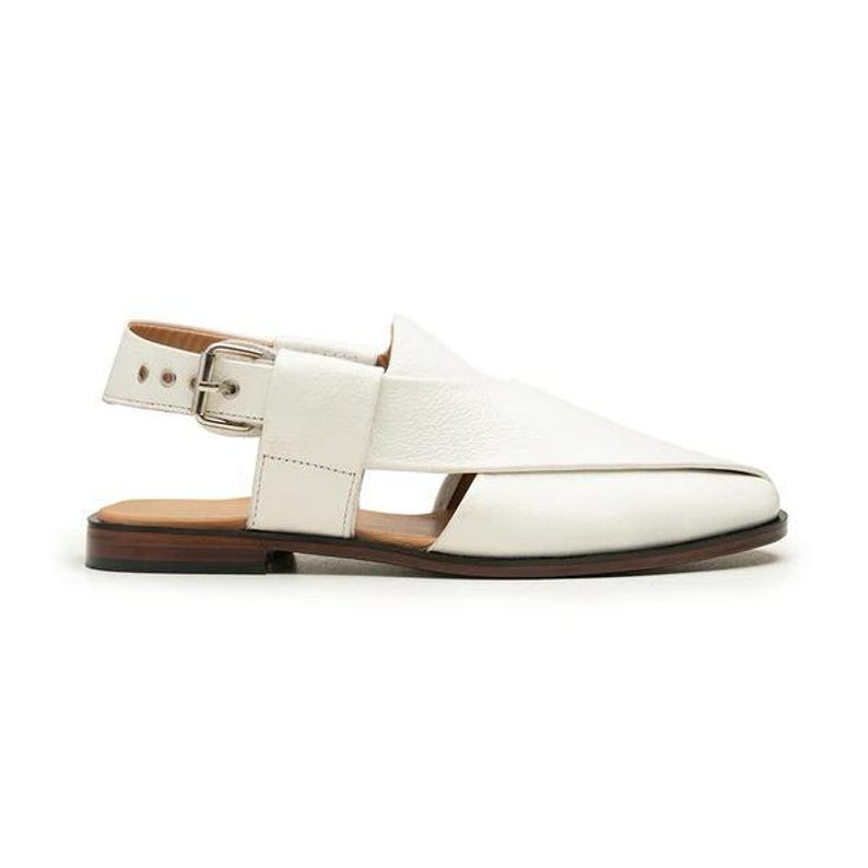 Op de afbeelding: Witte leren sandaal met een gespsluiting. De sandaal heeft een band over de bovenkant en een bruine zool. De schoen heeft een modern design en is geschikt voor casual wear.