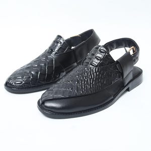 Pode incluir: Um par de sand&aacute;lias de couro preto com padr&atilde;o de pele de crocodilo. As sand&aacute;lias t&ecirc;m uma tira traseira e bico arredondado. Os sapatos s&atilde;o exibidos em um fundo branco.
