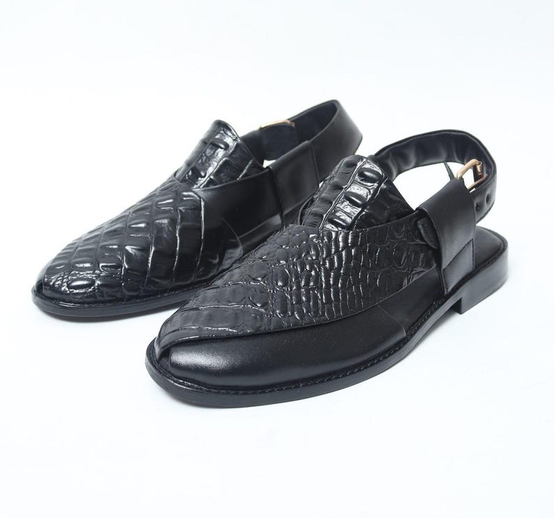 Pode incluir: Um par de sand&aacute;lias de couro preto com padr&atilde;o de pele de crocodilo. As sand&aacute;lias t&ecirc;m uma tira traseira e bico arredondado. Os sapatos s&atilde;o exibidos em um fundo branco.