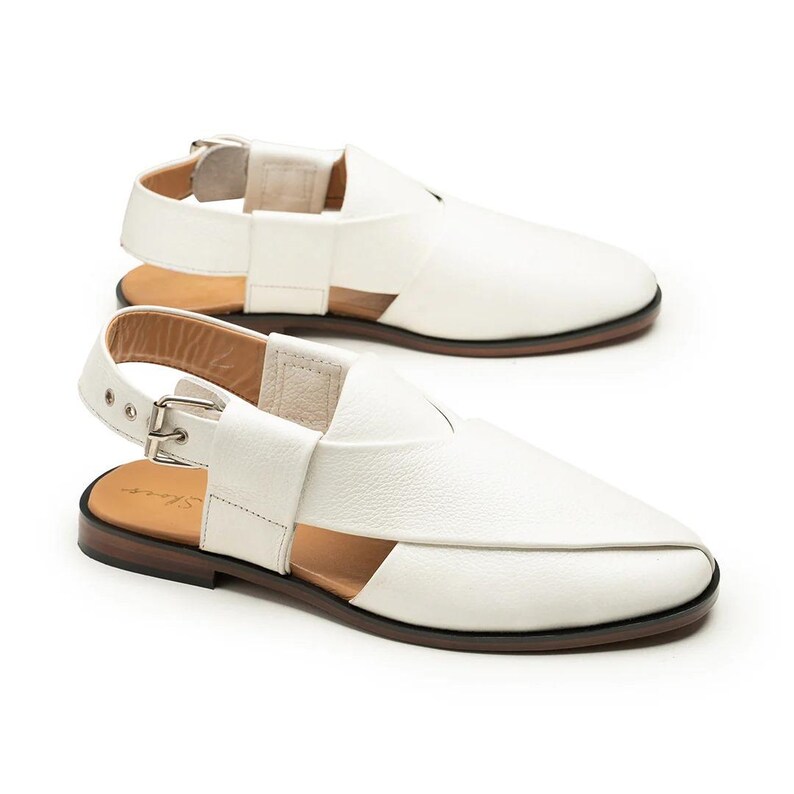 Op de afbeelding: Witte leren sandalen met een hielband en gespsluiting. De sandalen hebben een bruine zool en een uniek uitgesneden ontwerp. De schoenen worden gepresenteerd op een witte achtergrond.