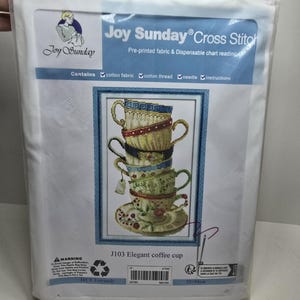 May include: A cross-stitch kit in a clear plastic package. The kit features a design of stacked teacups in various colors. The package includes the text "Joy Sunday Cross Stitch" and "Elegant coffee cup". The kit measures 15 x 21 inches.