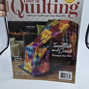 May include: A copy of "Love of Quilting" magazine. The cover features a colorful quilt with geometric patterns. The magazine's title is in large red letters, with text that reads "Harvest Hues: 11 Warm & Welcoming Patterns for Fall."