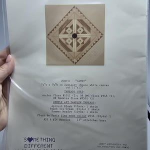 May include: A needlepoint pattern titled Cathy, featuring a geometric diamond design in shades of tan and brown. The package includes instructions for 7.5 inch by 7.5 inch canvas, thread requirements, and the Something Different brand logo.