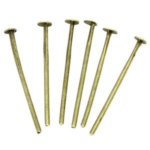 May include: Seven gold-colored metal pins with round heads. The pins are arranged in a fan shape.