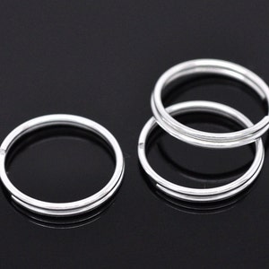 May include: Four silver key rings, each with a double loop design. The rings are stacked on top of each other.