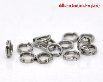 May include: A close-up of a pile of silver-toned jump rings. The rings are double-looped and have a dull finish. The text "dull silver tone (not silver plated)" is visible in the image.