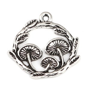 May include: Silver-toned pendant featuring three stylized mushrooms within a leafy wreath. The pendant has a loop at the top for easy attachment to a chain or cord. The design is detailed and suitable for jewelry making or crafting.
