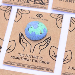 May include: A round, textured globe made of blue and green paper pulp containing wildflower seeds, attached to a rectangular brown card. The card features black line art of hands holding the globe, the text Company Name, and The Future Is Something You Grow.