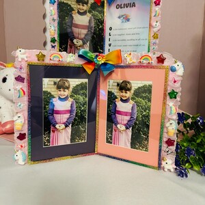 May include: A pink photo frame with a multi-colored bow and decorative embellishments. The frame holds three photos of a young girl. The frame is decorated with unicorns, rainbows, and stars. The name "OLIVIA" is written on the frame.