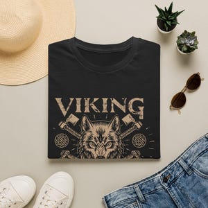 May include: Black t-shirt with a Viking theme. The shirt features the word "VIKING" in a distressed font above a wolf's head and crossed axes. The design is in shades of brown and tan.