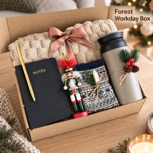 May include: A gift box labeled Forest Workday Box containing a beige textured blanket with a brown ribbon, a black notebook with the word NOTES, a gold pen, a nutcracker ornament, patterned socks, and a matte olive green travel mug with pine decor.