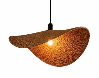 May include: A woven, brown pendant light fixture with a unique, curved design. The light has a black fixture and a single exposed lightbulb. The shade is made of a natural fiber material, creating a warm, inviting glow.