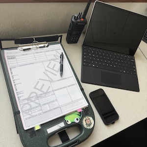 May include: A dark green plastic clipboard with a metal clip holding a Rapid Clinical Assessment form, a black pen, a black two-way radio with an antenna, a black tablet with a keyboard cover, and a black smartphone with a protective case.