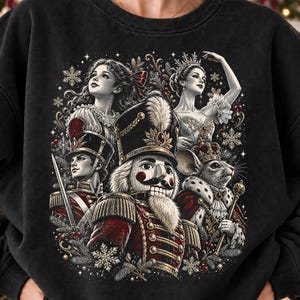 May include: A black crewneck sweatshirt featuring a detailed graphic print of characters from The Nutcracker, including a central nutcracker soldier, a mouse king, a ballerina, and a soldier with a sword, surrounded by snowflakes.