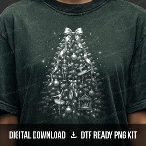 May include: A dark green mineral-washed t-shirt featuring a silver graphic of a Christmas tree decorated with a nutcracker, ballet dancers, pointe shoes, and ornaments. The design includes a large silver bow at the top and sparkling light effects.