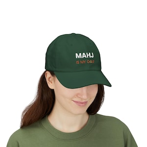 May include: A dark green baseball cap with the text "MAHJ IS MY GOLF" in white and orange. The cap has a curved brim and is made of a soft material.