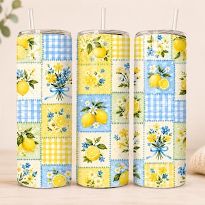 Könnte beinhalten: Drei zylindrische Becher mit durchsichtigen Deckeln und Trinkhalmen, die ein Patchwork-Design aus gelben Zitronen, blau-gelben Vichy-Karos und Sträußen aus kleinen blauen und gelben Blumen auf hellcremefarbenem Grund mit grünen Blättern zeigen.