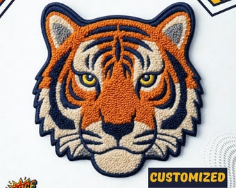 May include: Embroidered tiger head chenille patch in orange, navy blue, and cream colours. The patch features a detailed design with yellow eyes and the text "CUSTOMIZED CHENILLE PATCHES". The patch has a textured, raised appearance.
