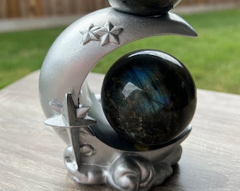 May include: Two iridescent labradorite spheres on a silver crescent moon stand. The moon has a star design on each side.