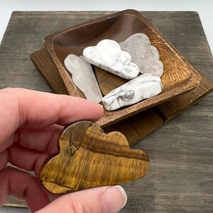 May include: A brown tiger's eye crystal carved in the shape of a cloud. The crystal is sitting on a wooden surface.
