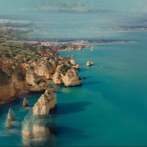 May include: Aerial view of a coastline with turquoise water and rocky cliffs. The cliffs are a light tan color, and the water is a vibrant blue. The sky is a pale blue with some clouds. The image has a natural, scenic feel.