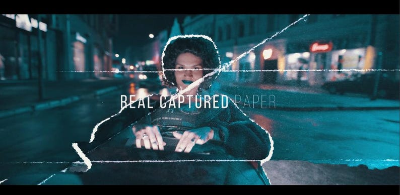 May include: A person with dark hair and blue lipstick is featured in a nighttime street scene. The image has a cinematic feel with the text "REAL CAPTURED PAPER" overlaid on the image. The background is blurred.