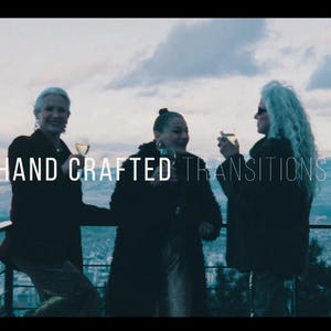 May include: Three people are standing on a balcony, holding glasses of a beverage, with a scenic view in the background. The text "HAND CRAFTED TRANSITIONS" is overlaid on the image. The sky is overcast.
