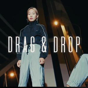 May include: A promotional image featuring three people wearing athletic wear. The central figure stands in light gray pants and a black jacket with white trim. The text "DRAG & DROP" is prominently displayed in white. The background is dark with architectural elements.
