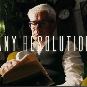 以下が含まれることがあります： メガネをかけた年配の人が明るい光の下で本を読んでいます。「ANY RESOLUTION」というテキストが大きな白い文字で表示されています。時計と植物のある薄暗い部屋が舞台です。