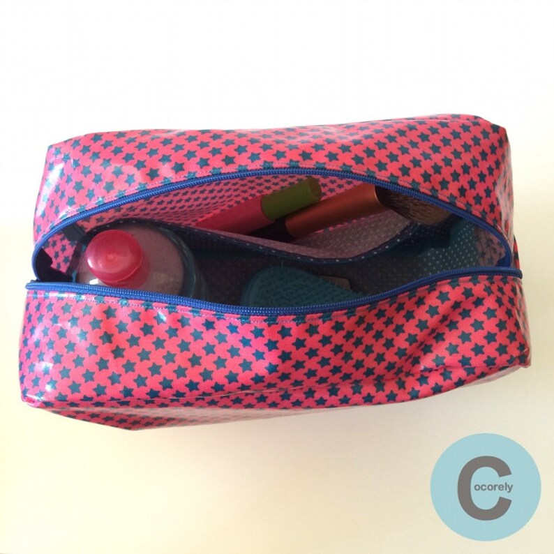 May include: A pink and blue zippered toiletry bag with a star pattern. The bag is open and contains a blue and green brush, a pink bottle, and a pink and brown makeup brush.