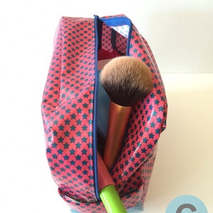 May include: A red and blue star-patterned zippered makeup bag with a blue zipper. The bag is open and contains a large makeup brush and a green tube of makeup.
