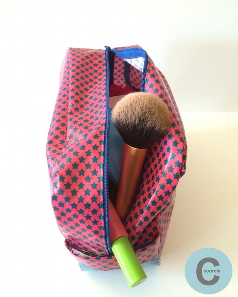 May include: A red and blue star-patterned zippered makeup bag with a blue zipper. The bag is open and contains a large makeup brush and a green tube of makeup.