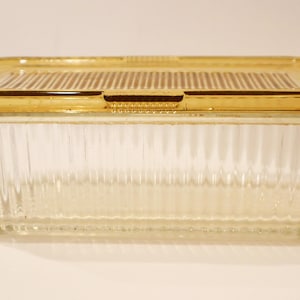 May include: A rectangular clear glass storage container with vertical ribbing along the sides and a matching amber-colored glass lid featuring a textured, striped pattern on the top surface. The container has a clean, functional design.