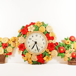 May include: A wall clock surrounded by a circular arrangement of sculpted red, yellow, and beige flowers with green leaves, flanked by two matching wall plaques featuring floral bouquets in brown woven baskets against a plain white background.