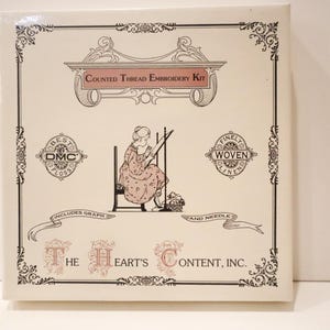 May include: A square off-white box for a Counted Thread Embroidery Kit by The Heart's Content, Inc. The front features black line art of a person stitching, DMC floss and linen labels, and text reading Includes Graph and Needle.
