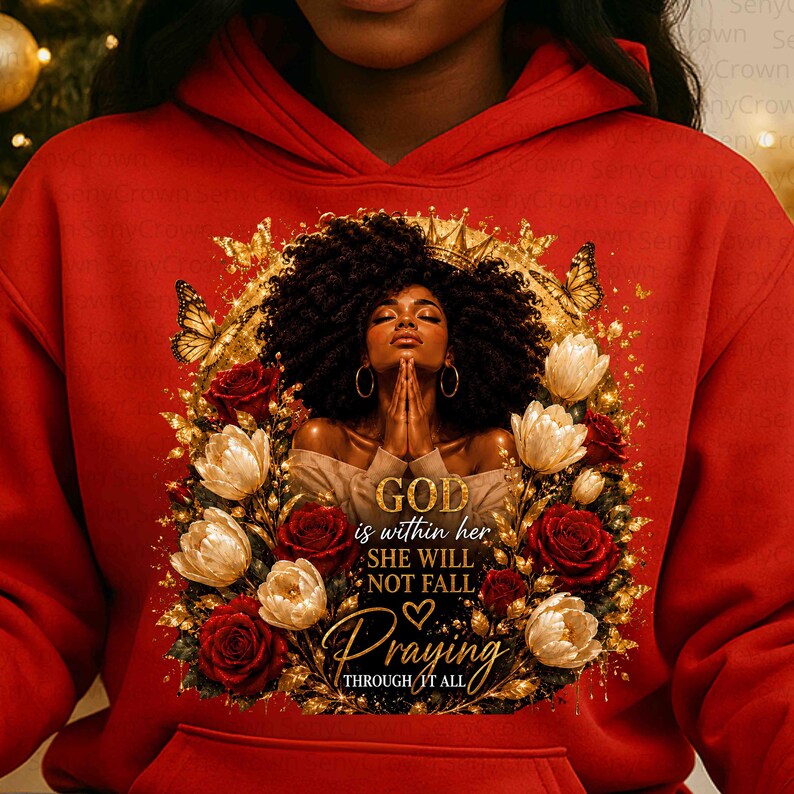 May include: A bright red hoodie featuring a graphic print of a person with dark curly hair and a crown, hands clasped in prayer, surrounded by gold butterflies and red and white roses. The text reads: GOD is within her SHE WILL NOT FALL Praying THROUGH IT ALL.
