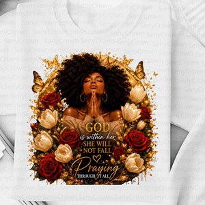 May include: A white t-shirt featuring a graphic print of a person with dark curly hair and a crown, hands clasped in prayer, surrounded by red roses, white tulips, and gold butterflies. The text reads: GOD is within her SHE WILL NOT FALL Praying THROUGH IT ALL.