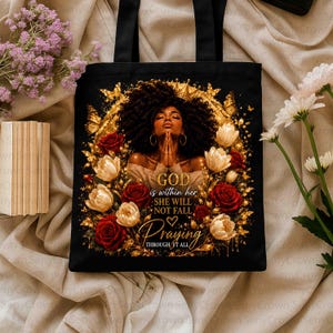 May include: A black tote bag featuring a graphic of a person with dark curly hair, surrounded by gold butterflies and red and white roses. The text reads: GOD is within her SHE WILL NOT FALL Praying THROUGH IT ALL. The design is framed in gold.