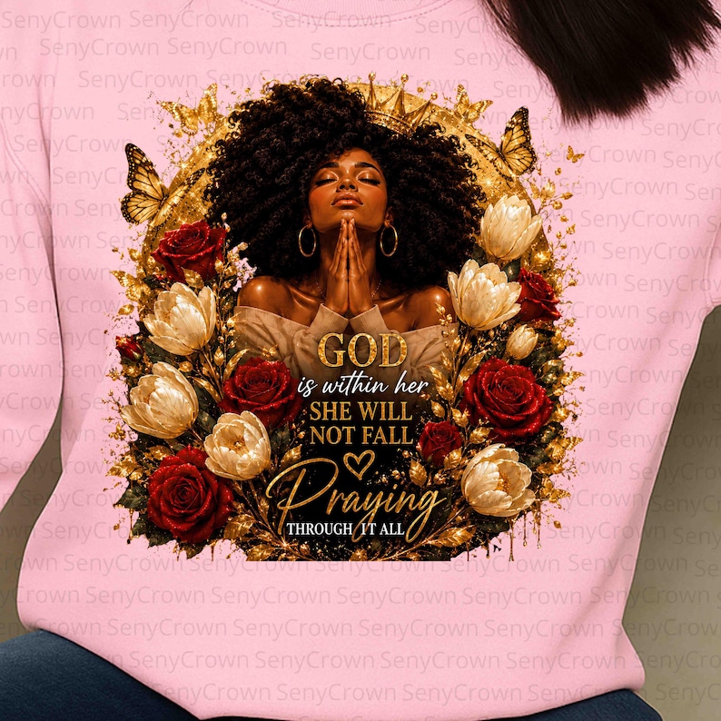 May include: A light pink sweatshirt featuring a graphic of a person with dark curly hair and a gold crown, framed by gold butterflies and red and white roses. The text reads: GOD is within her SHE WILL NOT FALL Praying THROUGH IT ALL.
