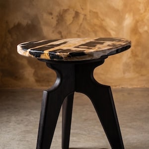 May include: A small, dark wood side table with an oval top. The tabletop has a striking black and tan pattern. The table has three angled legs. A small, neutral-coloured ceramic cup is next to it.