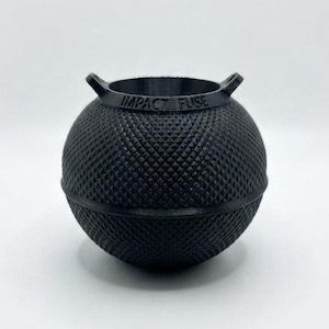 May include: A black spherical container with a textured diamond pattern on its surface. The top rim features two small protruding handles and the text IMPACT FUSE is embossed clearly on the upper edge of the object, which has a hollow centre.