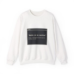 May include: A white sweatshirt with a black graphic that resembles a computer window. The text in the graphic reads "Works on my machine" followed by an error message. The sweatshirt has a crew neck and long sleeves.