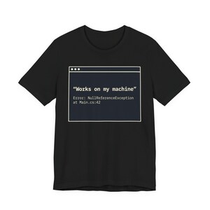 May include: Black t-shirt with a white framed graphic resembling a computer window. The graphic displays the text "Works on my machine" and an error message. A humorous design for computer programmers and developers.