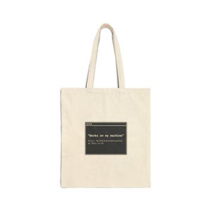 May include: A cream-colored tote bag with a black graphic of a computer window. The window displays the text "Works on my machine" and an error message. The bag has two handles and is made of a canvas-like material.