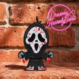 May include: A black and white figure with a ghost-like mask featuring red blood splatters, wearing a black hooded robe and holding two small knives with red tips. The text Dreamy Heavenly Scents is visible in a pink neon circle above the figure.