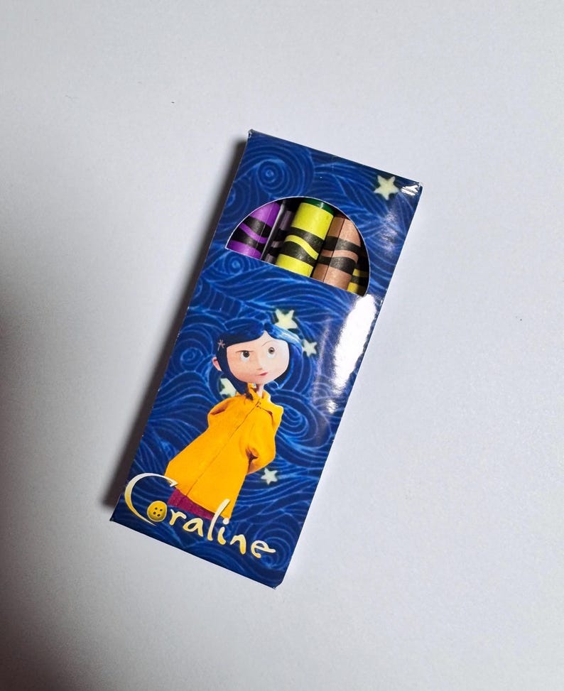 Op de afbeelding: Een rechthoekige doos met kleurpotloden op een blauwe achtergrond met wervelende patronen en gele sterren. De doos toont een personage met blauw haar in een gele regenjas en de tekst Coraline. Bovenaan zijn verschillende kleurpotloden zichtbaar.