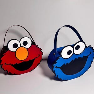 May include: Two character-themed bags, one red with an orange nose and the other blue. Both bags have large white-rimmed eyes and black mouths. Each bag has a matching handle for carrying.
