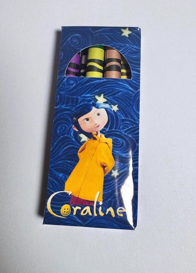 Op de afbeelding: Een rechthoekige doos met kleurpotloden op een blauwe achtergrond met wervelende patronen en witte sterren. Het personage Coraline, met een gele regenjas en blauw haar, staat op de voorkant met de tekst Coraline eronder. Bovenaan zijn de punten zichtbaar.