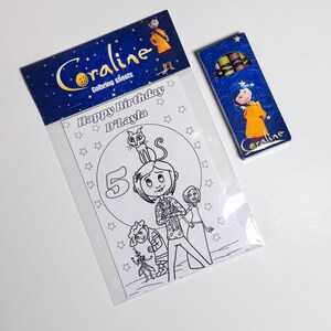 Op de afbeelding: Een kleurset met Coraline-thema in een doorzichtige plastic verpakking met een blauwe kopkaart met de tekst Coraline coloring sheets, inclusief een Happy Birthday D'Layla kleurplaat met personages en een klein doosje met kleurpotloden.
